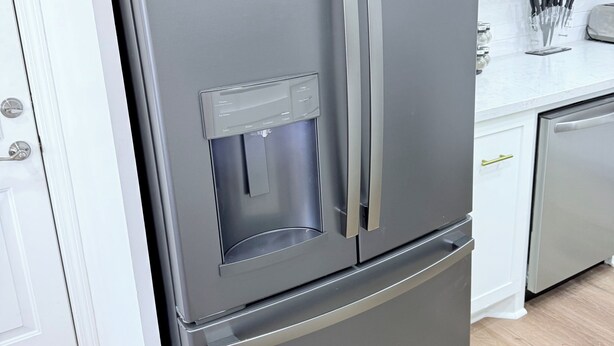 Een roestvrijstalen koelkast met een water- en ijsdispenser, in een keuken met witte kasten en een houten vloer.