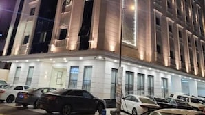 Et hotel med flere etager og en moderne facade, med store vinduer og en parkeringsplads med flere biler.