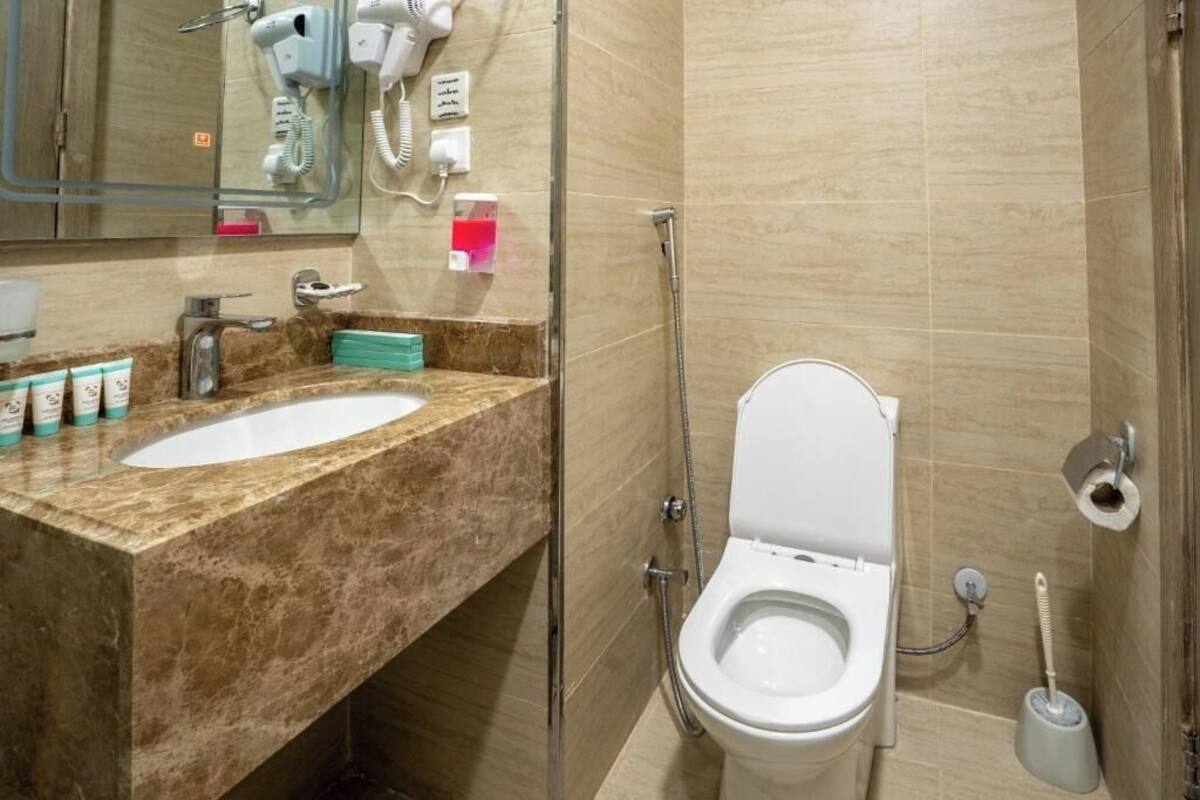 A bathroom with a marble sink, a toilet, a handheld showerhead, and a hairdryer mounted on the wall.