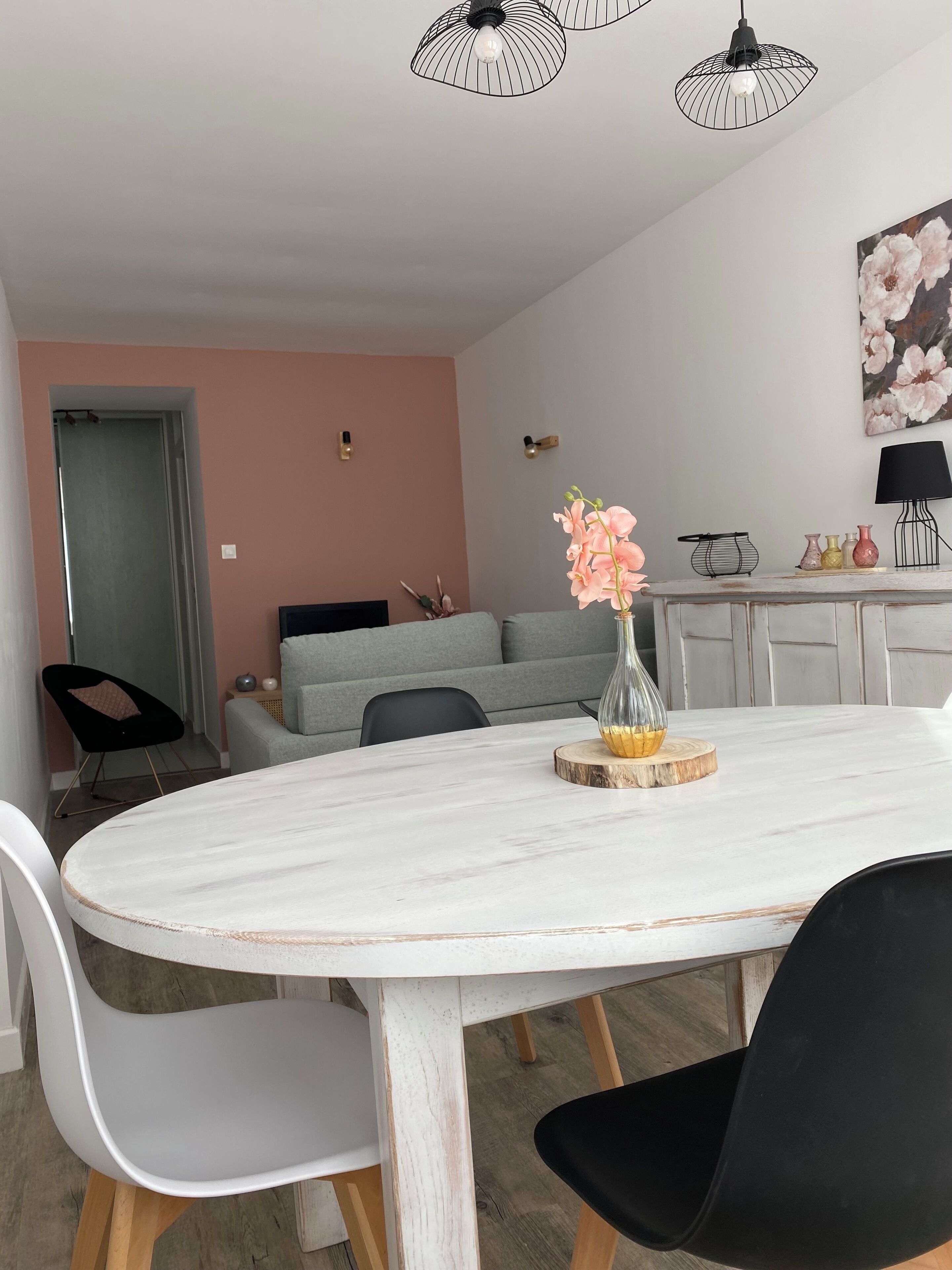 A dining area with a white marble table, black chairs, a vase with flowers, and a grey sofa in the background.