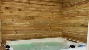 Une cabane en bois avec un jacuzzi, des portes coulissantes grises et un banc en bois.