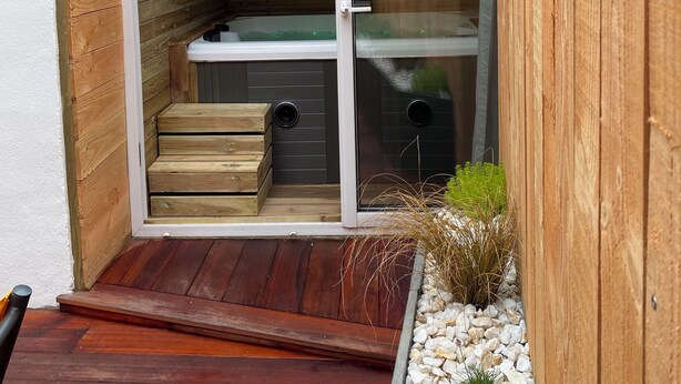 Un espace extérieur compact, construit en bois, doté d’une porte-fenêtre coulissante, d’un petit coin salon et d’une terrasse en bois.