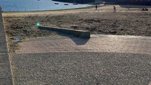 Une plage avec un ciel dégagé, quelques bateaux et des bâtiments en arrière-plan.