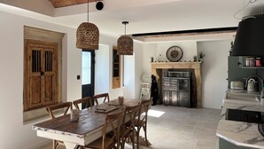 Un coin repas avec une table et des chaises en bois, un plafond en briques et une cheminée surmontée d’une étagère.