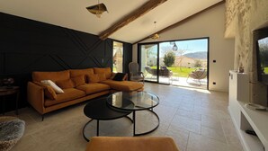 Un salon moderne avec un canapé d’angle, une table basse en verre et une grande porte-fenêtre coulissante donnant sur une terrasse extérieure.