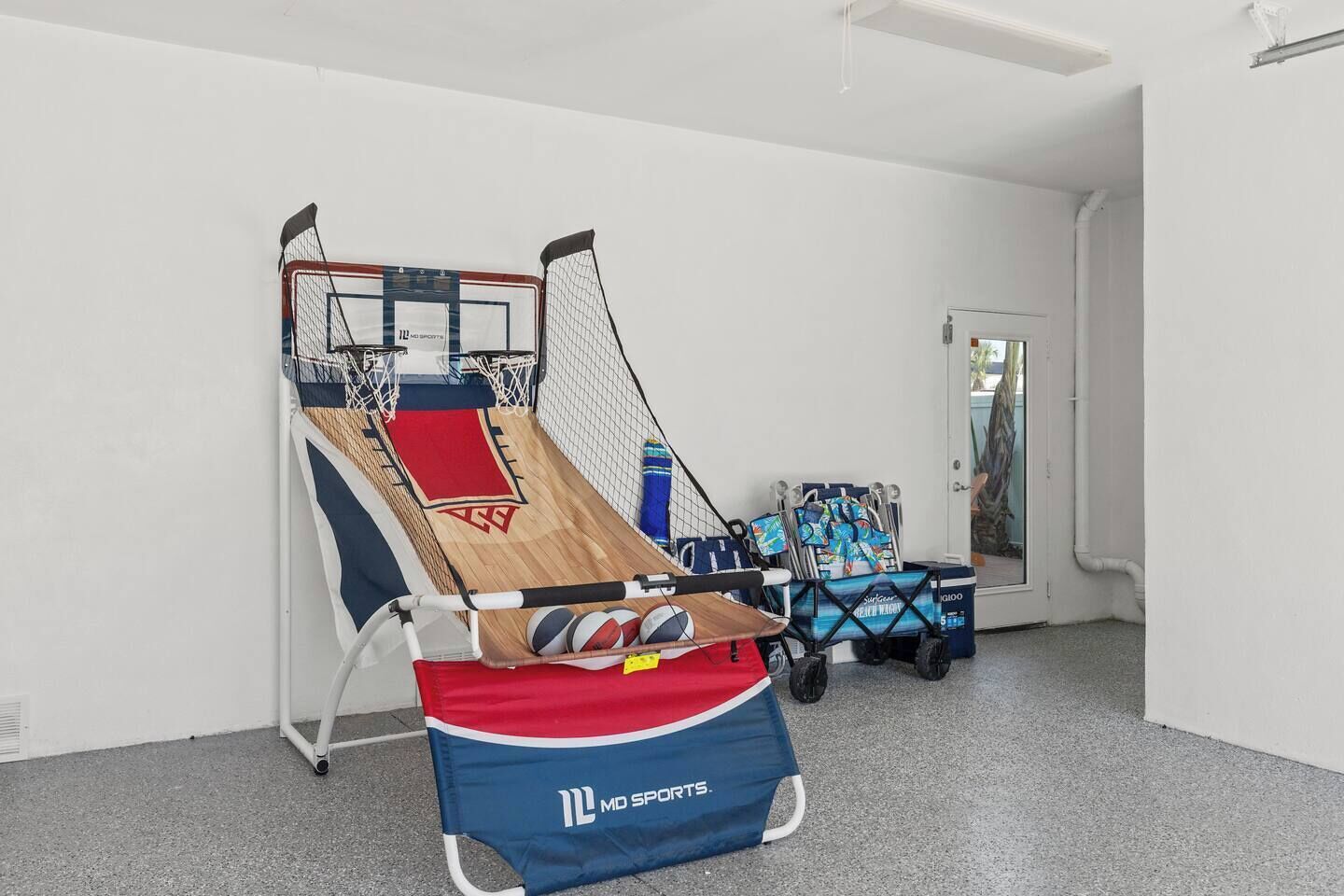 A basketball court with a net, a red and blue mat, and a cart with sports equipment.
