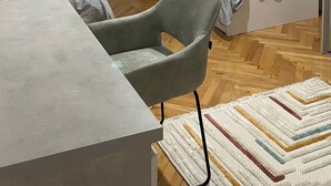 A small, well-lit room with two beds, a chair, a table, and a patterned rug. - Modern City Apartment (Bitola)