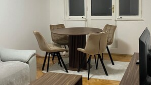 A modern living room with a round dining table, beige chairs, a sofa, a TV, and a ceiling light. - Modern City Apartment (Bitola)