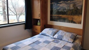 A bedroom with a bed, a wooden cabinet, a window with a view of trees and a car, and a painting of a landscape on the wall. - Mountain Paradise - a private guest suite in Flagstaff (Flagstaff)