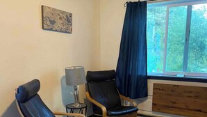 A room with two leather chairs, a small table with a lamp, a window with blue curtains, and a wooden bench. - Mountain Paradise - a private guest suite in Flagstaff (Flagstaff)