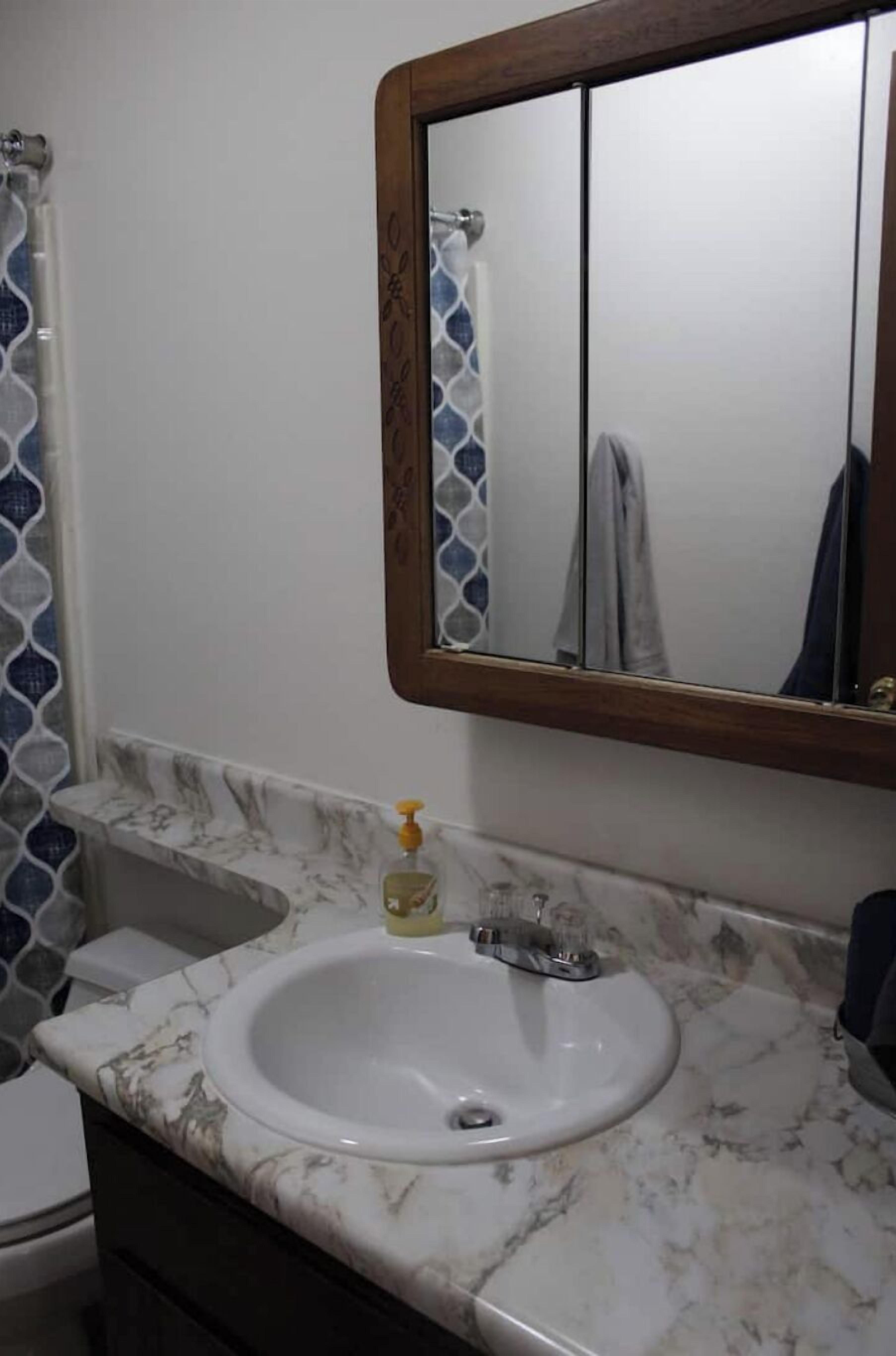 A bathroom with a marble sink, a mirror, and a shower curtain.