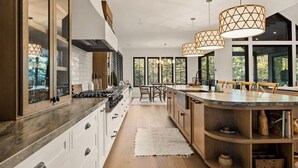 A modern kitchen with a central island, large windows, and pendant lighting.