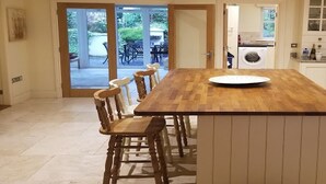 A kitchen with a wooden table, chairs, a clock, and a view of the outdoors.