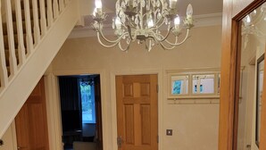 A spacious hallway with a chandelier, wooden doors, and a patterned rug.