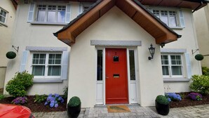 A two-story building with a red door, white shutters, and a brick pathway leading to the entrance.