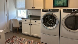 Una cocina pequeña con muebles blancos, lavadora y una silla.