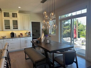 A modern kitchen with white cabinets, a dark wooden dining table, and a large sliding glass door leading to an outdoor patio.