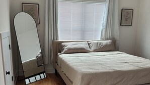 A bedroom with a bed, a large mirror, a window with blinds, and wooden flooring. - Nashville Rodeo House (Nashville)