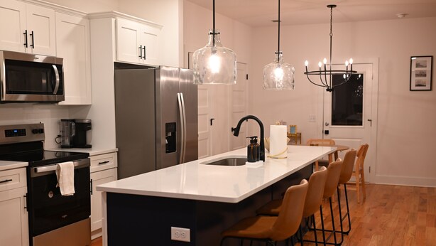 A modern kitchen with stainless steel appliances, a central island with bar stools, pendant lighting, and a large window. - Nashville Rodeo House (Nashville)