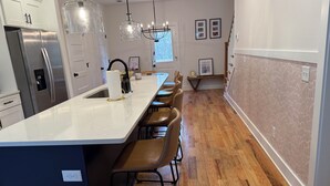 A modern kitchen with a central island, bar stools, stainless steel appliances, pendant lighting, and a patterned wall. - Nashville Rodeo House (Nashville)
