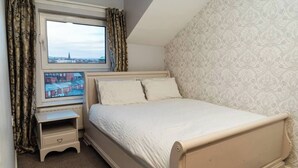 Un dormitorio con cama, mesita de noche, ventana con cortinas y un papel pintado estampado.