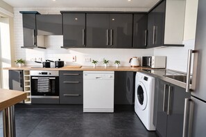 A modern kitchen with stainless steel appliances, a dishwasher, a washing machine, and a wooden countertop.