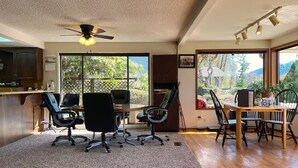 A spacious room with a large dining table, multiple chairs, a ceiling fan, and a view of a garden through large windows. - 1 Bedroom Retro Riverside Home with view ! (Sultan)