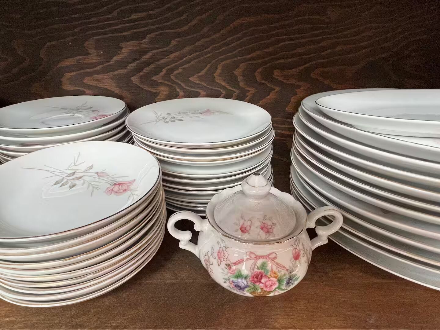 Stacks of white plates and a floral teapot on a wooden surface.