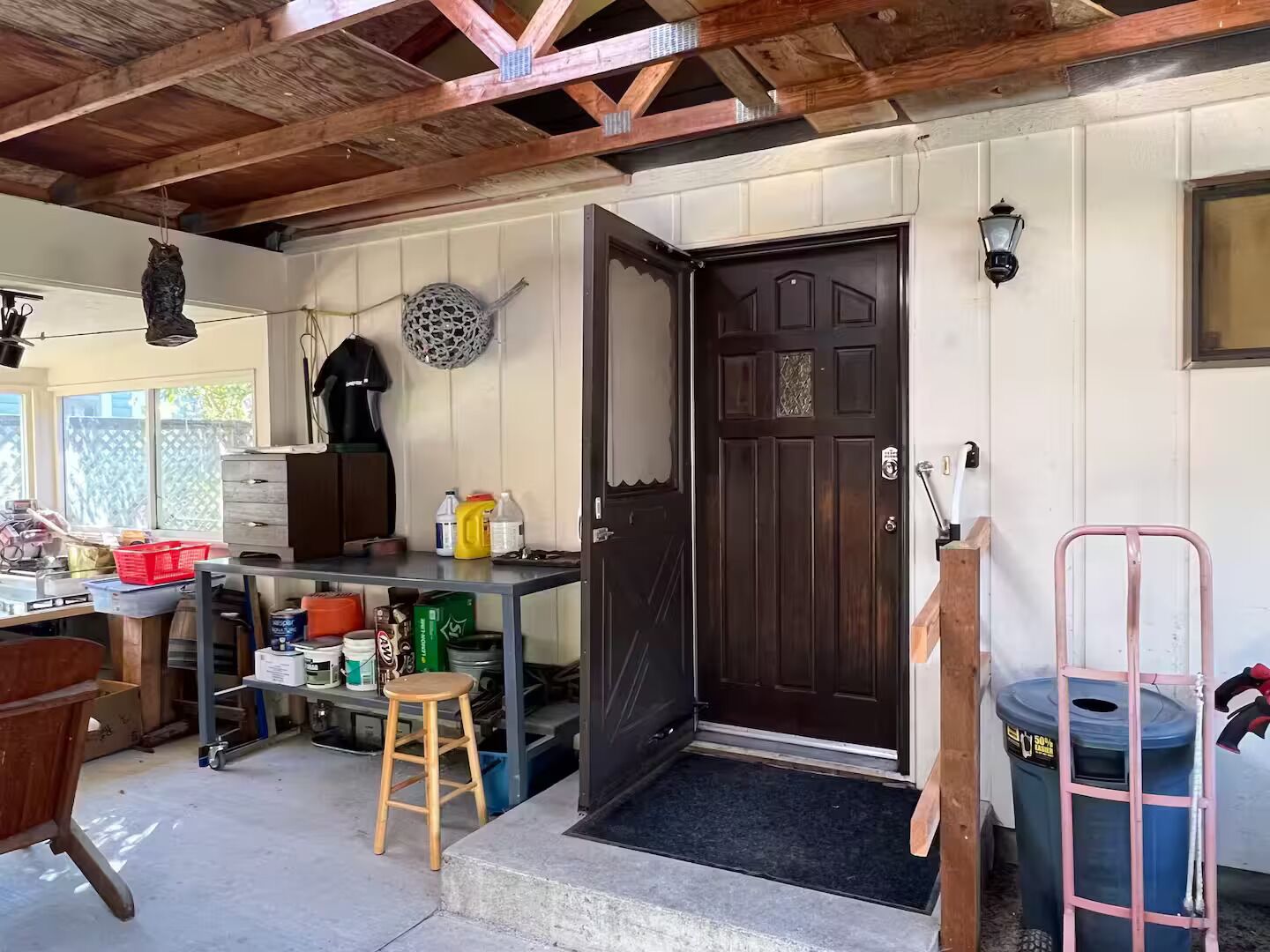 A rustic kitchen with a wooden ceiling, a black door, and a small stool.
