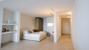 Ein modernes Hotelzimmer mit Bett, Nachttisch, Lampe und einer kleinen Küchenzeile.