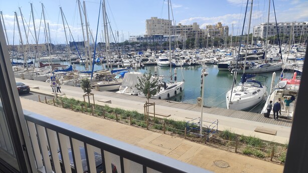 Un puerto deportivo con numerosas embarcaciones amarradas, un paseo peatonal y vistas de los edificios circundantes.