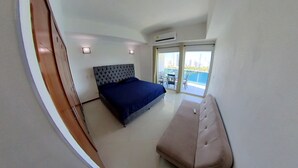A bedroom with a bed, a bench, a wardrobe, and a balcony with a view. - apartamento de 2 habitaciones (Cartagena de Indias)