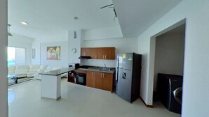 A modern kitchen with wooden cabinets, a refrigerator, and a microwave. There is a dining area with a white table and chairs. - apartamento de 2 habitaciones (Cartagena de Indias)