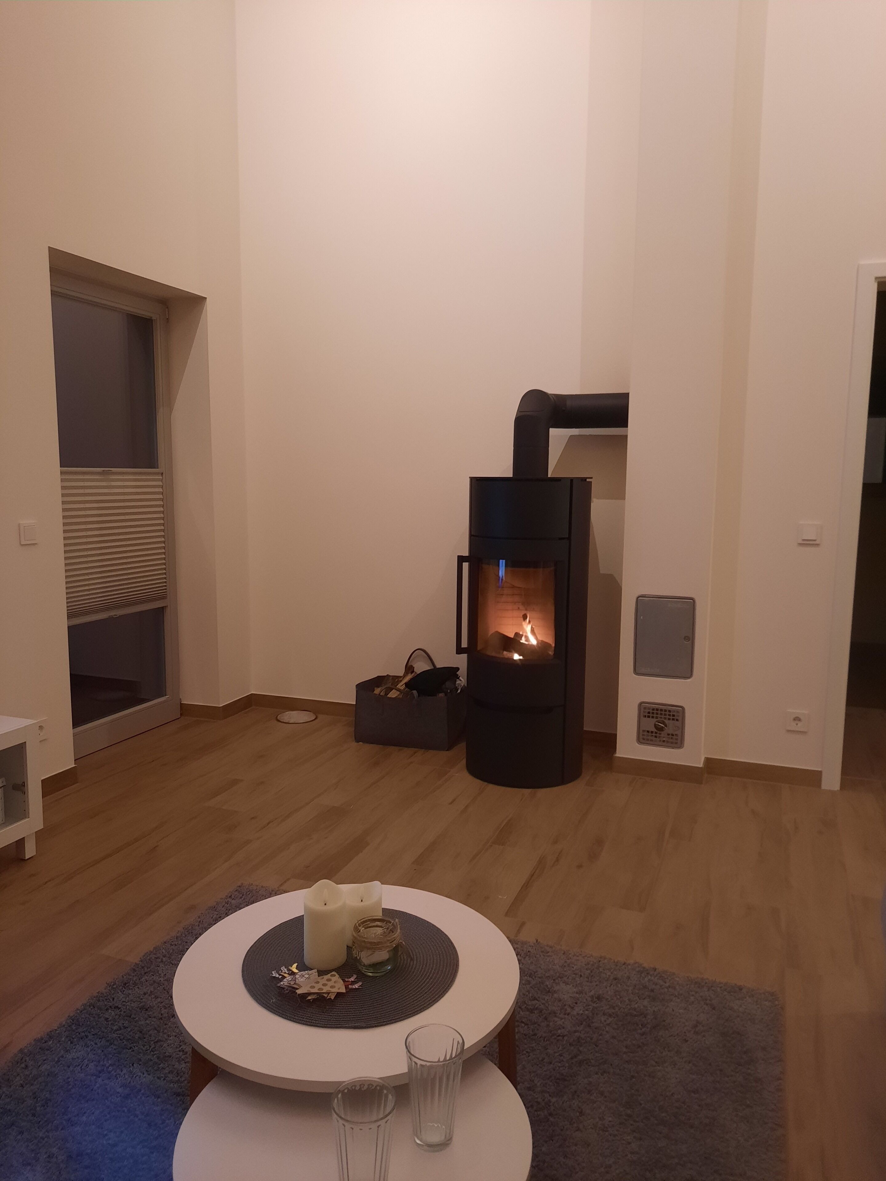 A living room with a wood-burning stove, a round table with candles, and a glass.