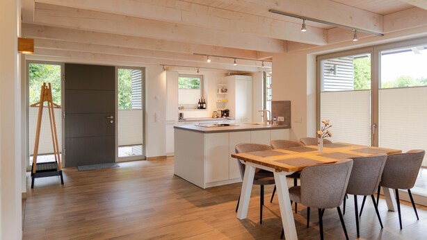 A modern kitchen with a central island, a dining area with a wooden table and chairs, and large windows providing natural light. - Vacation home Neukalen on Lake Kummerow - ideal for families and small groups (Neukalen)