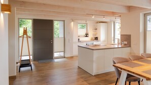A modern kitchen with a central island, wooden flooring, and a dining area with a table and chairs. - Vacation home Neukalen on Lake Kummerow - ideal for families and small groups (Neukalen)