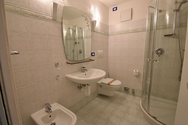 A bathroom with a glass-enclosed shower, a pedestal sink, a toilet, and a mirror.
