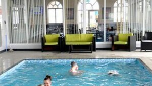 A swimming pool with people in the water, indoor seating, and large windows. - Abi Caravan Sleeps 8 Lyons Winkups Holiday Park (Abergele)