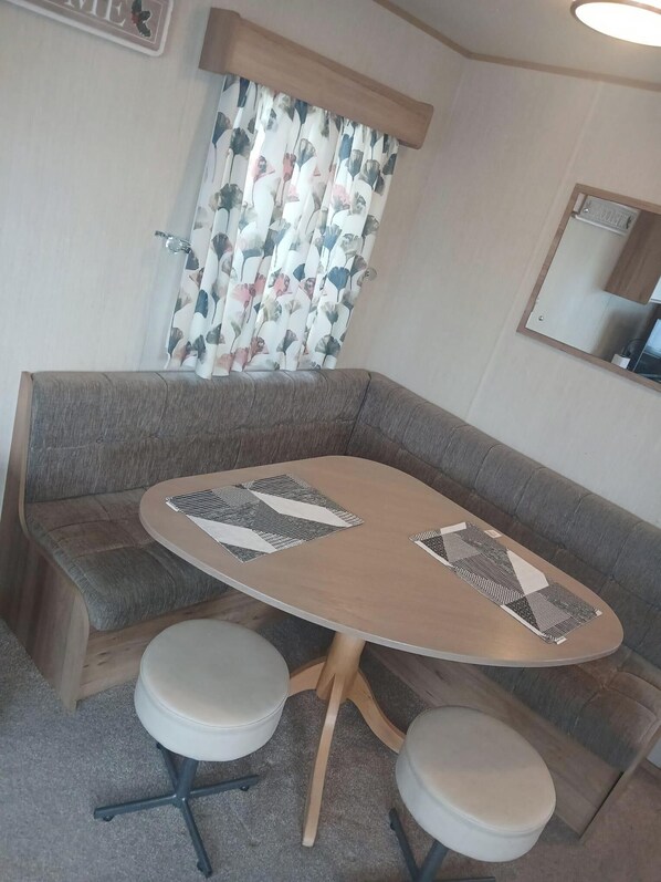 A compact living space with a sofa, a small round table, and two matching stools. A curtain with a floral pattern is partially drawn, and a mirror is mounted on the wall.