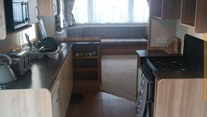 A compact RV kitchen with wooden cabinets, a stove, a sink, and a window overlooking a residential area. - Abi Caravan Sleeps 8 Lyons Winkups Holiday Park (Abergele)