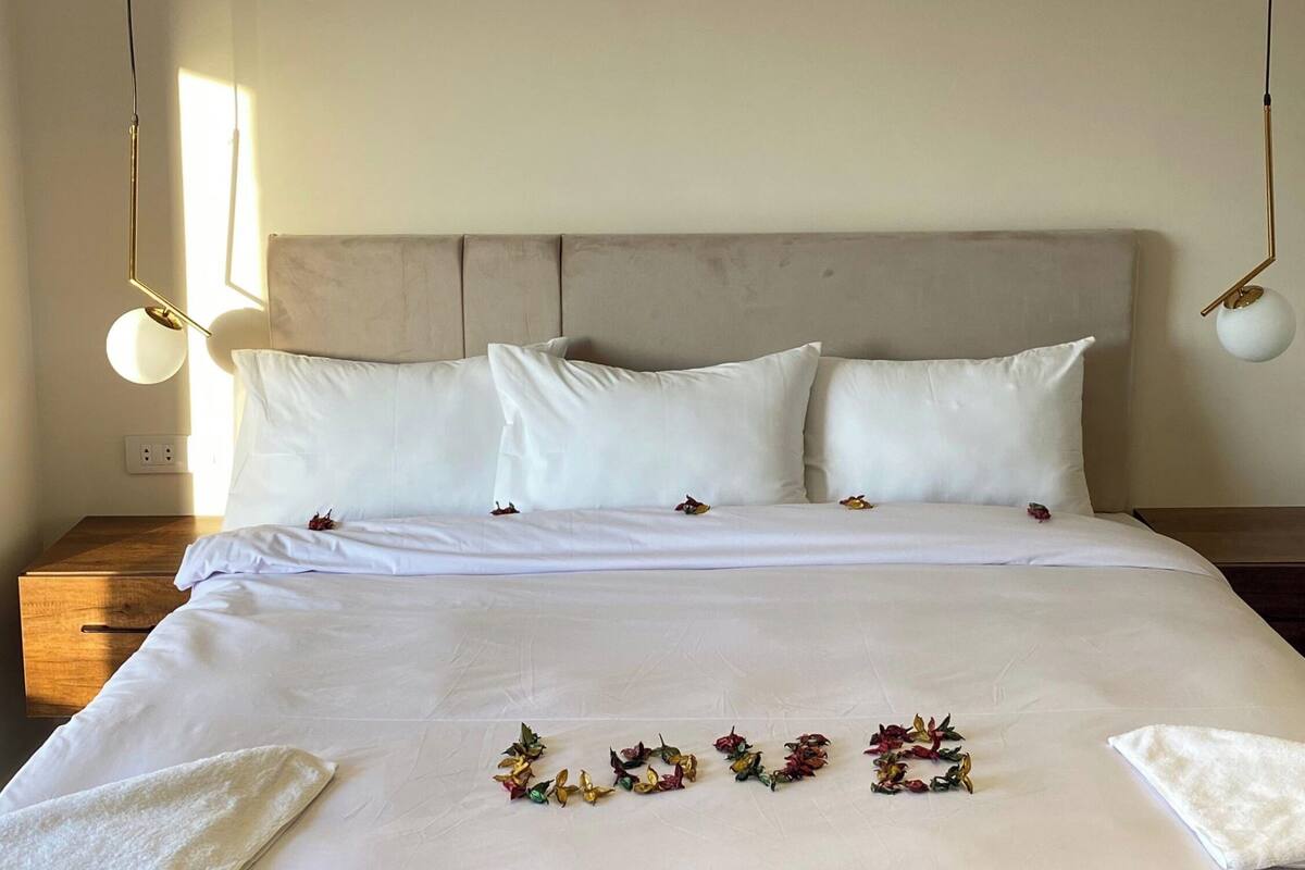A bedroom with a bed, white bedding, a headboard, and an air conditioning unit on the wall.