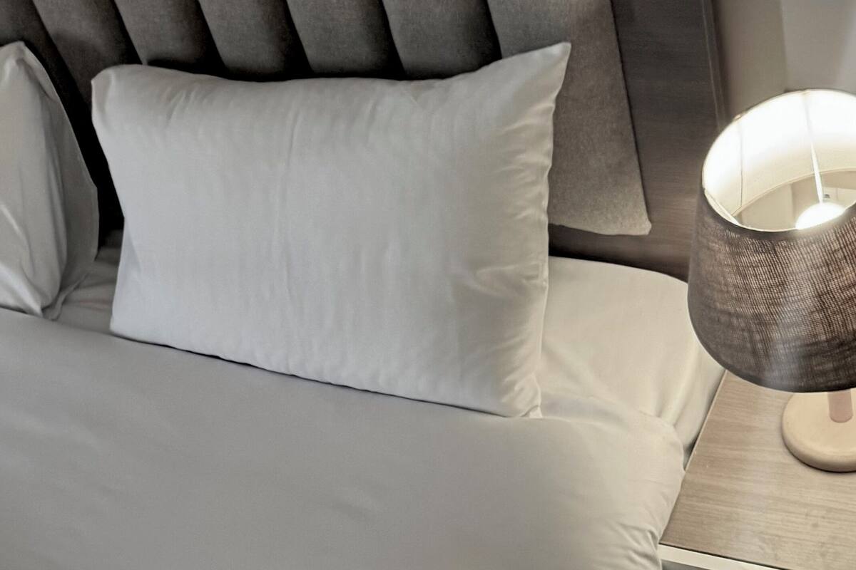 A neatly made bed with white linens and a grey upholstered headboard.
