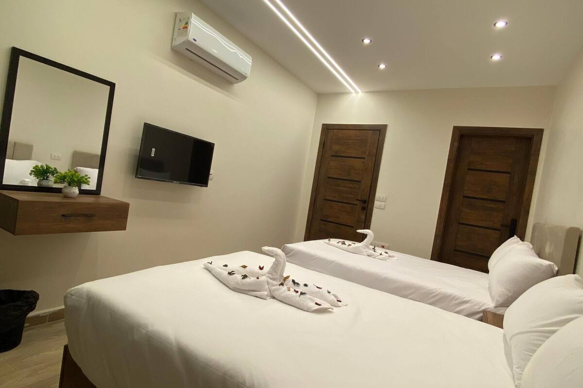A hotel room with two beds, a flat-screen TV, an air conditioning unit, and a wooden door.