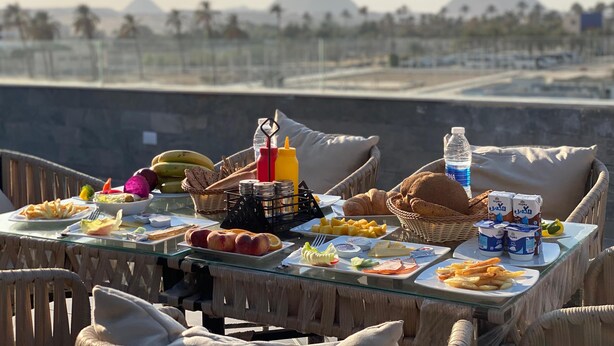 A table set with food and drinks, overlooking a view of pyramids. - Galleria Pyramids View Hotel (Giza)