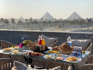 A table set with food and drinks, overlooking a view of pyramids. - Galleria Pyramids View Hotel (Giza)