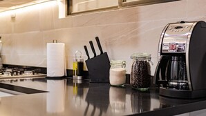 Une cuisine moderne équipée d’une cuisinière à gaz, d’une machine à café, d’un bloc à couteaux et de pots contenant des grains de café et du sucre.