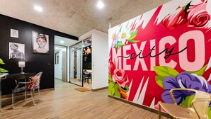 Un intérieur moderne agrémenté d’une fresque représentant le mot « MEXICO » et de motifs floraux, d’un plancher en bois et de chaises transparentes.