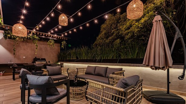 Un espace extérieur aménagé avec des meubles en osier, des guirlandes lumineuses et un grand parasol.