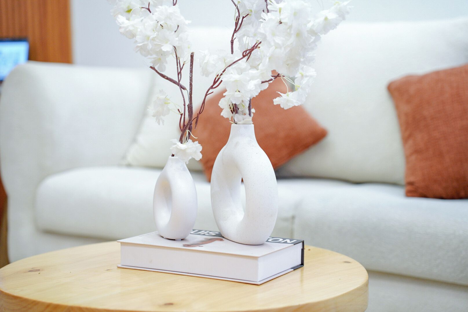 A round wooden table with two white vases and a book on it.