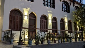 A building with multiple arched windows and balconies, surrounded by potted plants and a paved walkway. - Eyaru Palace  (Luxor)